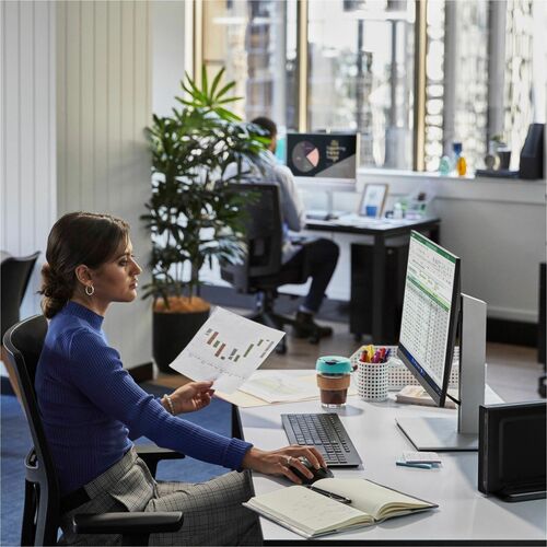 Woman working at a desk in an office with a computer and documents.