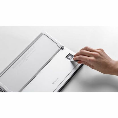 Hand placing a small square device onto a larger electronic device on a white surface