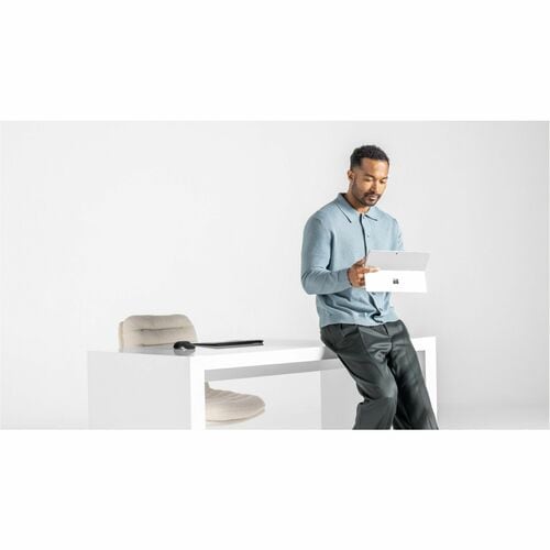 Man sitting on a white chair holding a laptop with a minimalistic background