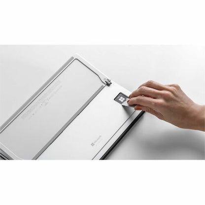 Hand placing a small square device onto a larger electronic device on a white surface