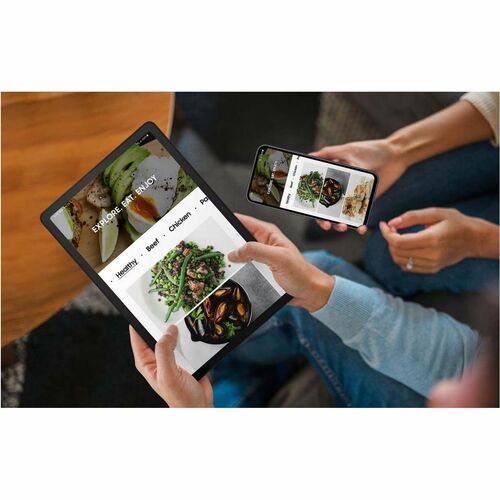 Two people using digital devices to view a food delivery app on a wooden table.