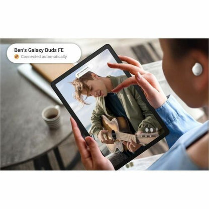 Person holding a tablet with a guitar player on screen, wearing a white earbud.