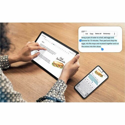 Person using a tablet and smartphone with text input on a wooden table